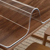 A clear PVC table protector mat is shown draped over a wooden table surface.