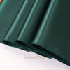 A close-up of a dark emerald green satin table runner rolled and draped.