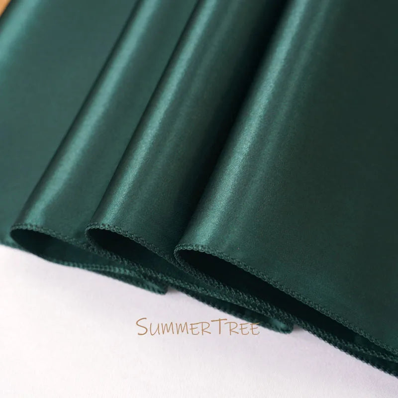 A close-up of a dark emerald green satin table runner rolled and draped.