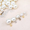 A collection of small, round, off-white pearl beads and silver eye screw pins for jewelry making.