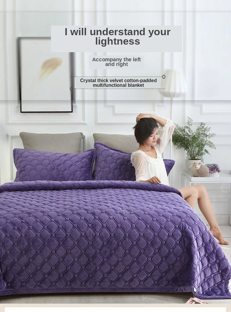 A purple plush velvet quilted blanket is displayed on a bed, with a woman sitting beside it.