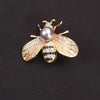 A gold-toned crystal bee brooch featuring a pearl accent and pave-set stones on the wings.