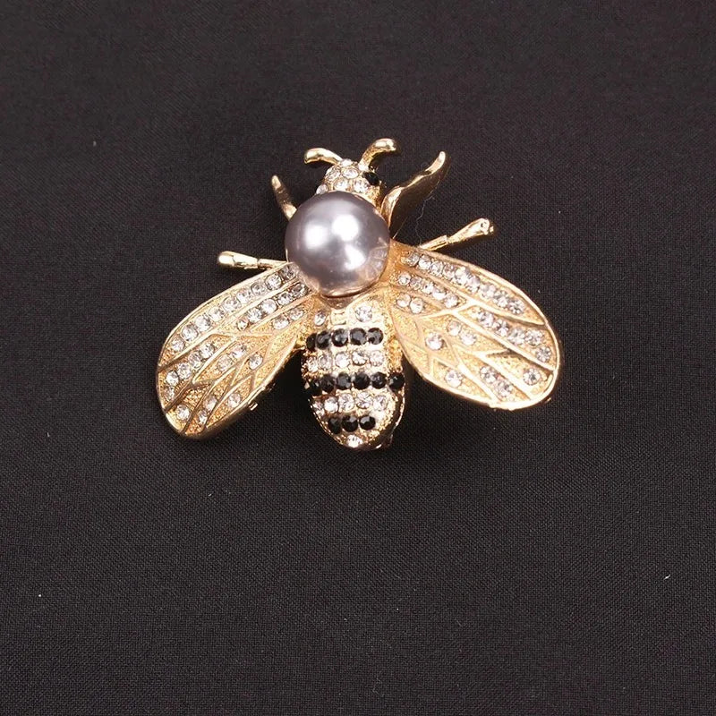 A gold-toned crystal bee brooch featuring a pearl accent and pave-set stones on the wings.