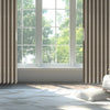 A modern interior featuring a light gray sofa and a wooden armchair next to a large window with vertical pleated curtains.
