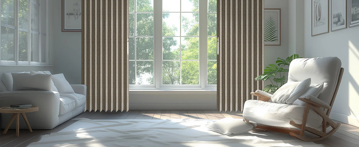 A modern interior featuring a light gray sofa and a wooden armchair next to a large window with vertical pleated curtains.