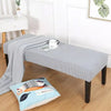 A gray elastic stool cover draped over a wooden bench in a bright living room setting.
