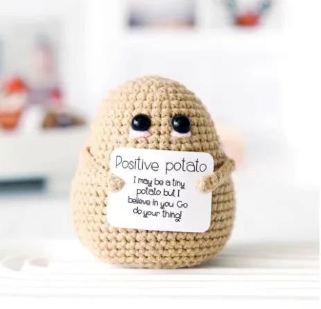 A handmade beige plush pocket doll with a sign that reads Positive potato