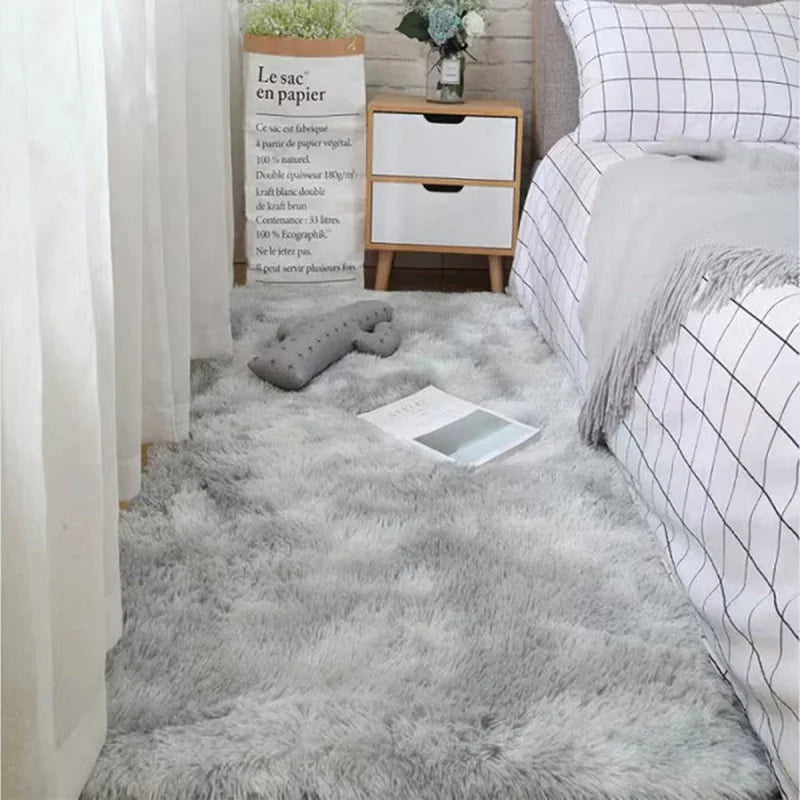 A fluffy gray silk wool floor rug placed in a bedroom setting next to a white cabinet and bedding.