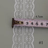 A close-up view of a white floral lace ribbon with a brown cotton trim and a ruler for scale.