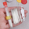 A hand holds a clear glass bottle containing a set of stainless steel embroidery and knitting needles with a gold ring.