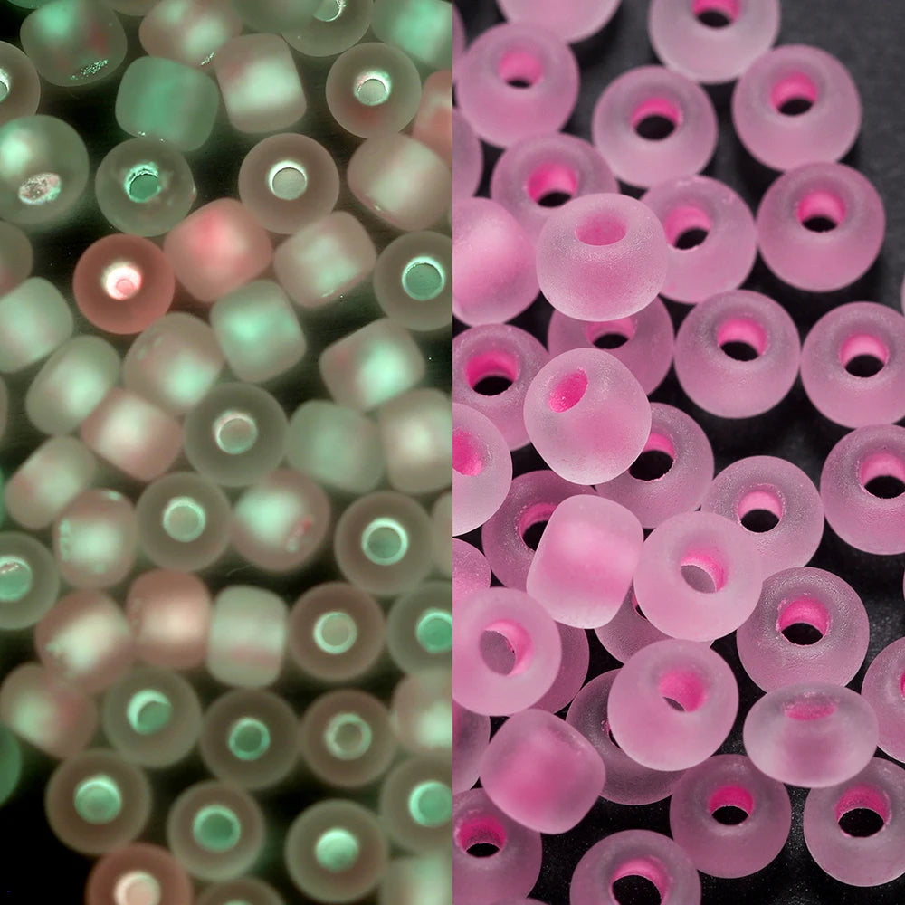 A close-up view of a 600-pack of 3mm glow-in-the-dark glass seed beads in various shades of pink and green.