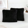 Two black faux fur throw pillows resting on a white sofa next to a framed picture.