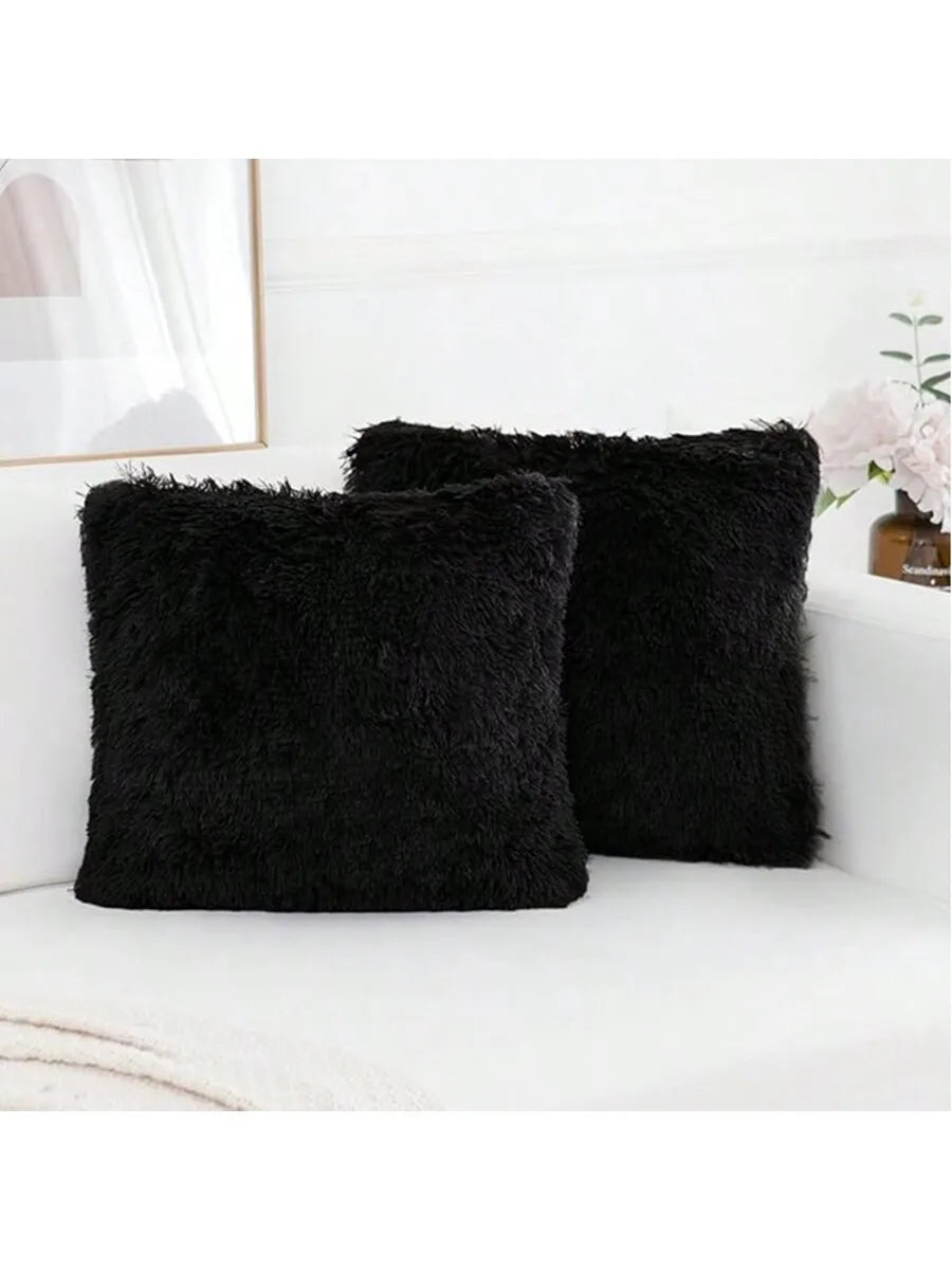 Two black faux fur throw pillows resting on a white sofa next to a framed picture.