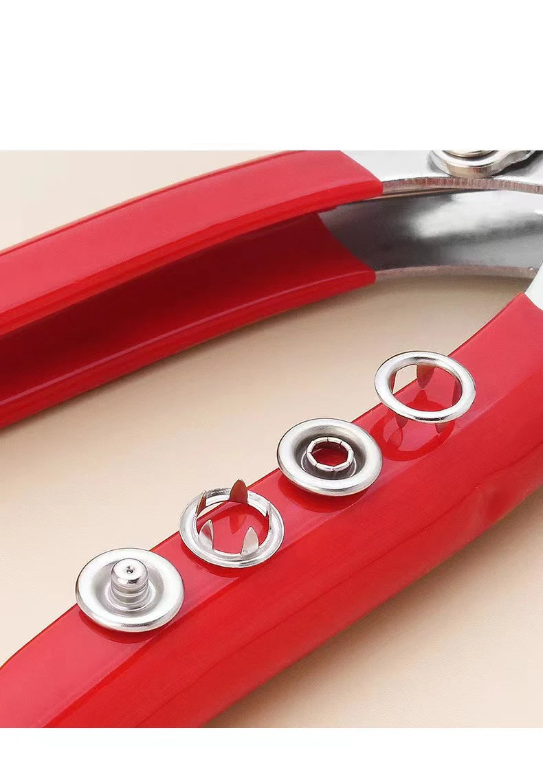 A close-up view of a red metal sewing button kit with various silver buttons and a metal tool.