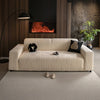 A cream-colored stretchable sofa cover with a vertical line pattern sits on a light rug in a modern, dark-toned room.
