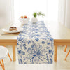 Blue and white porcelain floral linen table runner displayed on a wooden table with fresh greenery.
