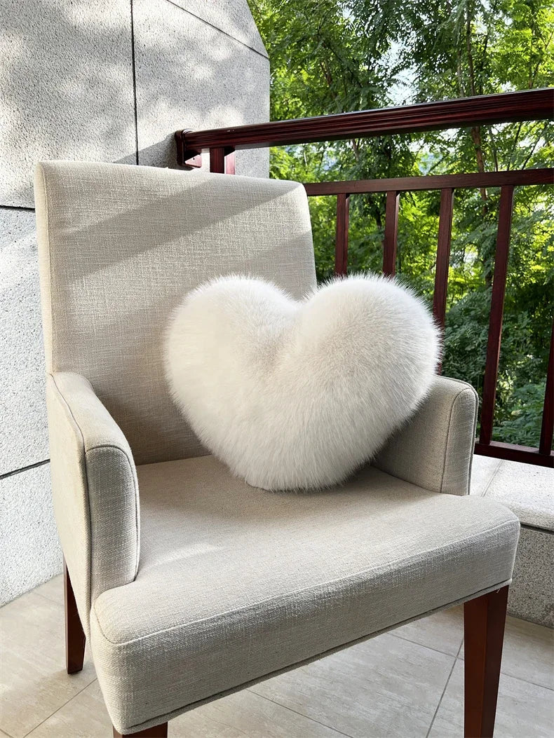 A light beige upholstered armchair with a fluffy white heart-shaped fox fur throw pillow on a balcony.