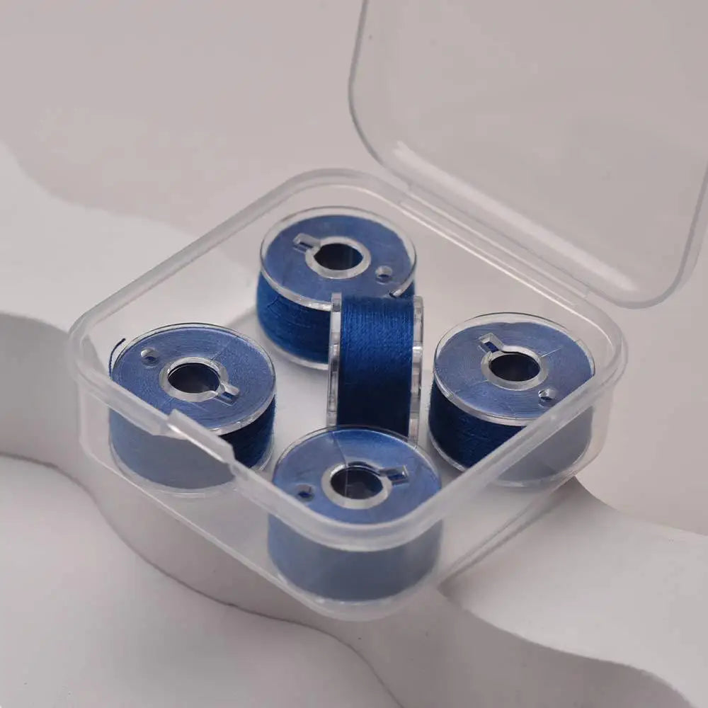 A clear plastic container holds several blue prewound sewing machine bobbin threads.