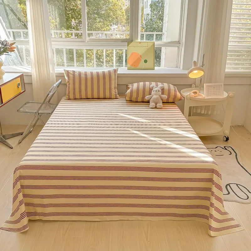 A bed dressed with striped organic cotton bedding, featuring a beige and reddish stripe pattern.