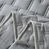 A close-up of a light gray quilted fabric, likely bedding, showing the stitching and texture.