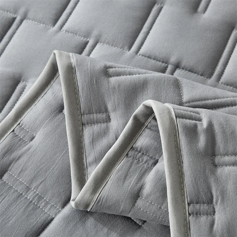 A close-up of a light gray quilted fabric, likely bedding, showing the stitching and texture.