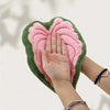 A hand is holding a green and pink plant-shaped towel with textured fibers.