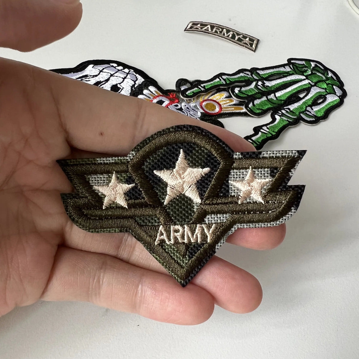 A hand holds a military style embroidered patch featuring a star and the word ARMY on a dark green background.