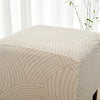 A close-up of a beige geometric jacquard ottoman slipcover with curved lines.