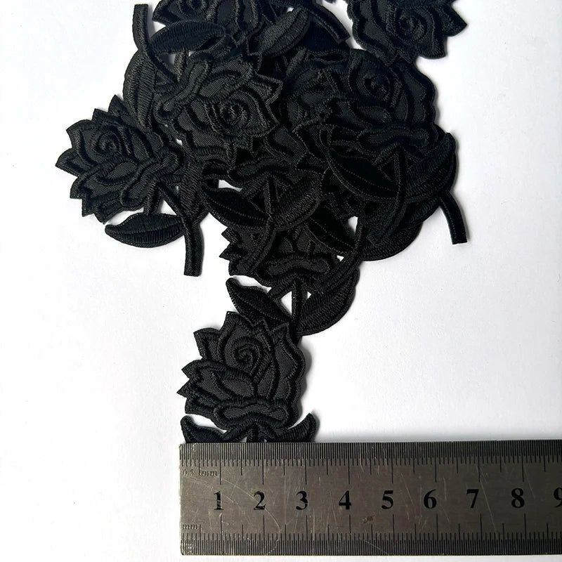 A cluster of black embroidered rose flower patches shown next to a ruler for scale.