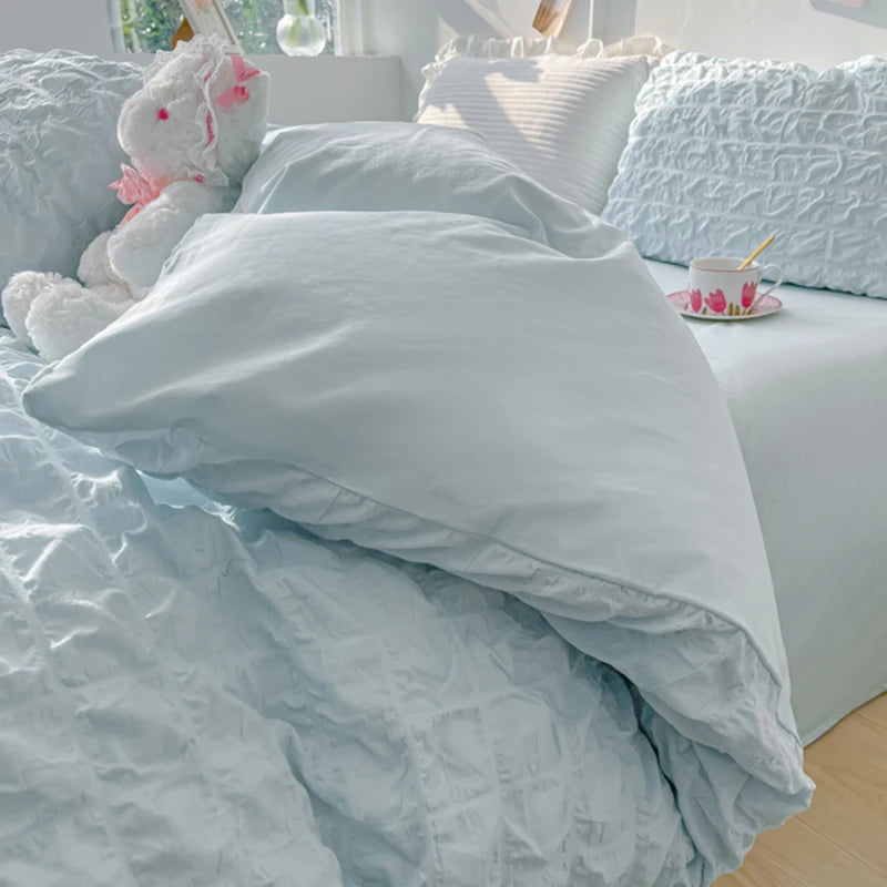 A close-up of a light blue textured duvet cover set with white pillows and pink accents on a bed.