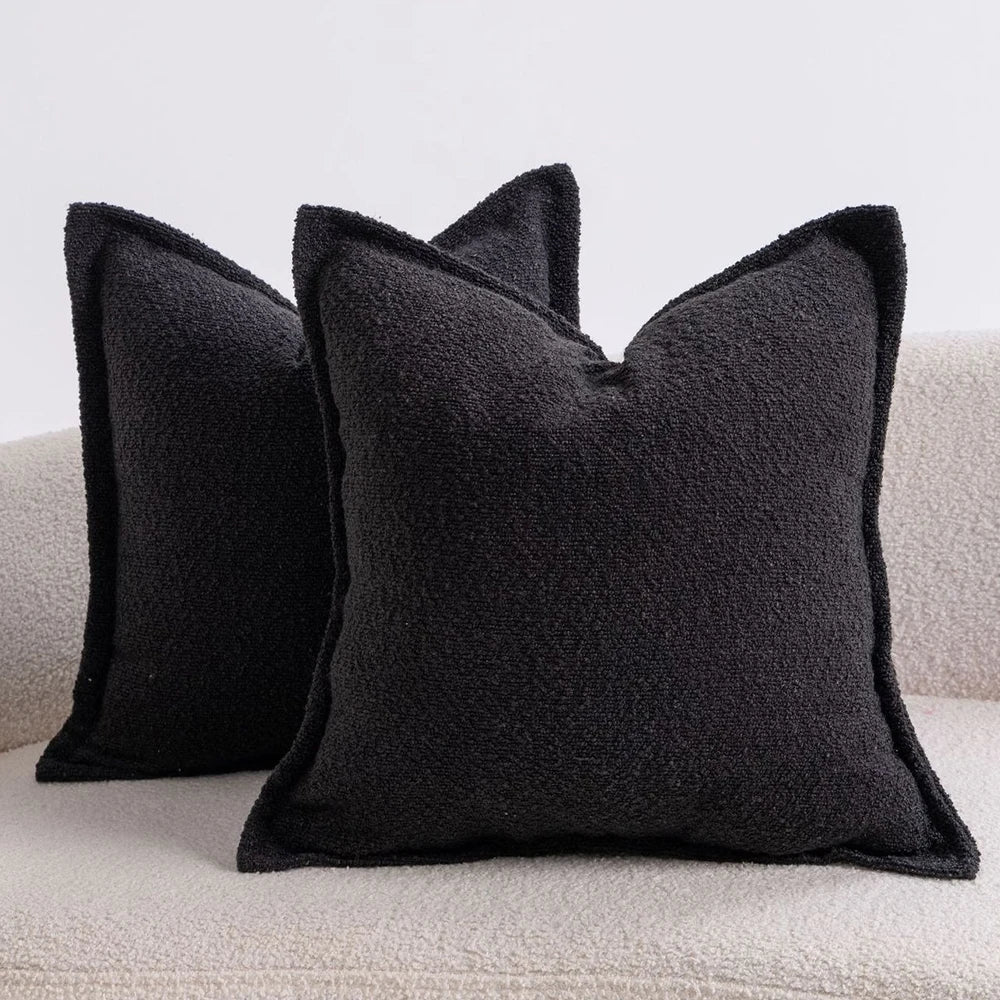 A black textured boucle throw pillow resting on a light-colored sofa.