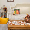 Linen table runner with autumn decor featuring gourds and leaves on a wooden table.