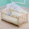 A wooden foldable mosquito net canopy with a light green fabric covering an infant cot.