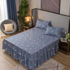 A gray bed with a blue printed skirt and pillows in a bedroom setting.