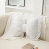 White embroidered sofa cushion with lace trim and fluffy fabric draped on a light-colored sofa.