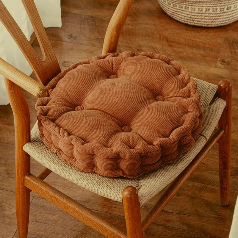 A brown tufted corduroy floor seat cushion rests on a wooden chair frame.