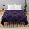 A purple gothic damask throw blanket draped over a bed with white pillows and a wooden nightstand.