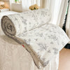 A rolled and unfolded white quilt blanket with a floral print resting on a white bed.