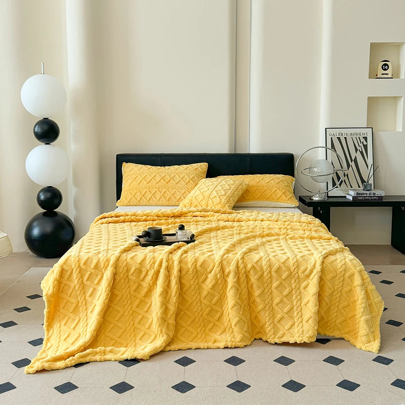 A bright yellow quilted coral fleece blanket spread on a bed, next to a black sofa and white decor.
