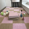 A pink and beige checkered play mat with soft plush EVA foam tiles and a white lamp in the background.