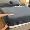 A hand is folding a dark gray luxury velvet bedding set onto a bed.