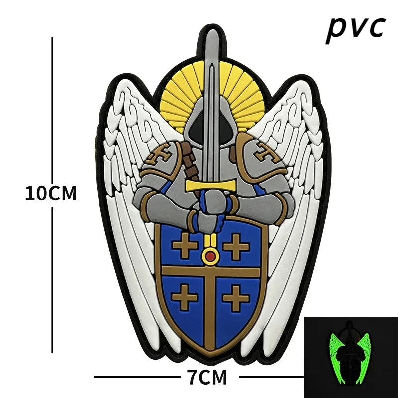 An embroidered angel patch featuring white wings, a golden sunburst, and a blue shield with crosses on a black background.