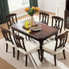 A dark wood dining table set with matching chairs and a vase of orange flowers in a bright room.