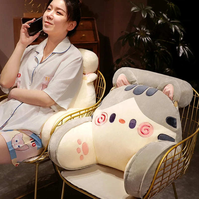 A woman is sitting on a gold-framed chair with a large, light gray animal plush sofa cushion.