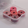 A clear plastic container holding several pink and red prewound sewing machine bobbin threads.