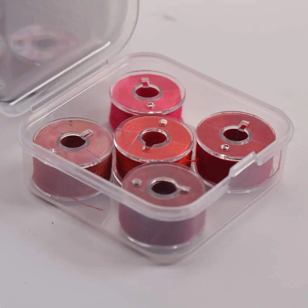 A clear plastic container holding several pink and red prewound sewing machine bobbin threads.
