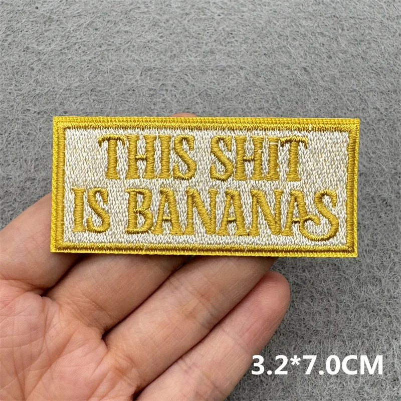A yellow embroidered patch with the text THIS SHIT IS BANANAS is held in a hand.
