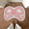 A pink fabric bow shaped rug is placed on a wooden floor next to a person's feet.