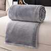 A stack of gray flannel throw blankets rolled and folded on a white sofa.