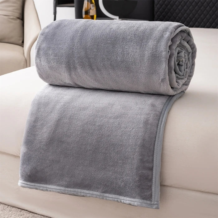 A stack of gray flannel throw blankets rolled and folded on a white sofa.